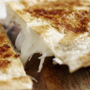 Gros plan d'un PLATEAU DE MINI PITA AU FROMAGE (barquette de 20 pièces) montrant des mini-pitas dorés et croustillants que l'on sépare pour révéler le fromage gluant et fondu qui s'étend entre les morceaux sur une surface en bois.