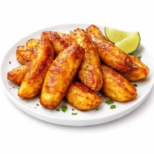 ALOKO (Minimum de commande 30 pièces) : Des bananes plantains rôties et dorées sur une assiette blanche, garnies d'herbes vertes et accompagnées de deux quartiers de citron vert, le tout sur un fond blanc uni.