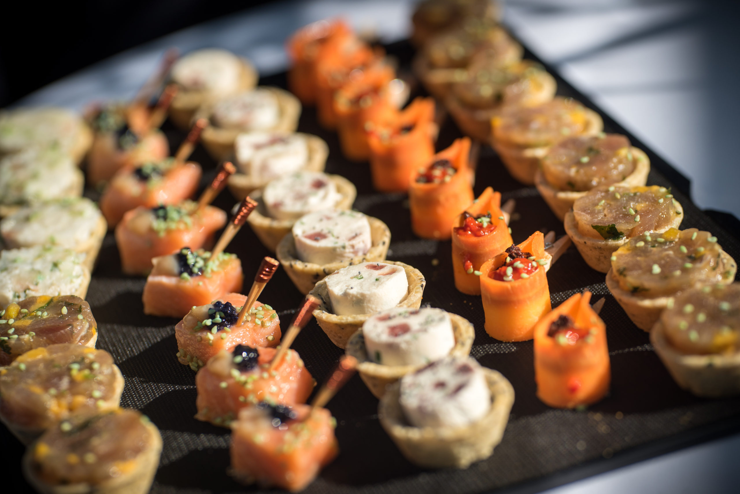 Gros plan sur un plateau rempli d'amuse-gueules assortis, comprenant des mini-tartes, du saumon fumé roulé et des roulés de carottes, tous garnis d'herbes et d'épices.