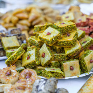 PLATEAU DE PATISSERIES ORIENTALES (10 pièces) présentant un assortiment de pâtisseries du Moyen-Orient, telles que des baklavas fourrés aux pistaches et des friandises à base de noix, joliment disposées sur des assiettes sur un marché ou dans une boulangerie.