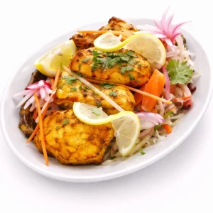 BOLYWOOD KEBAB (300g) : Morceaux de poulet marinés et grillés, garnis de citron et de coriandre, servis dans une assiette ovale blanche avec des oignons émincés, des carottes, des radis et une salade de chou frais.