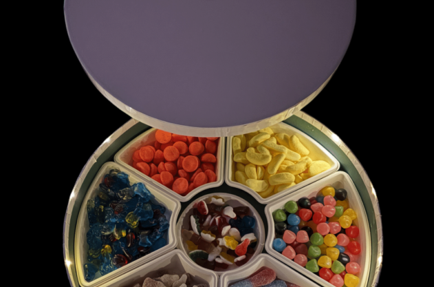 Un récipient rond avec un couvercle violet, divisé en sections contenant des bonbons colorés assortis, y compris des gommes, des bonbons à la gelée, de la réglisse et d'autres sucreries.