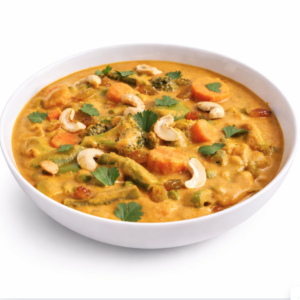 Un bol blanc rempli de KORMA ROYAL DE LÉGUMES crémeux (250 g), garni de coriandre et de noix de cajou. Les ingrédients visibles sont des carottes, des haricots, des brocolis et des petits pois. L'arrière-plan est blanc.