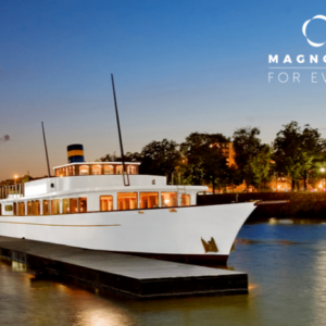 Un yacht blanc, LE YACHT CLIPPER (75015), est amarré à une jetée au crépuscule, avec les lumières de la ville et des arbres en arrière-plan. Le logo Magnolia For Event apparaît dans le coin supérieur droit de l'image.