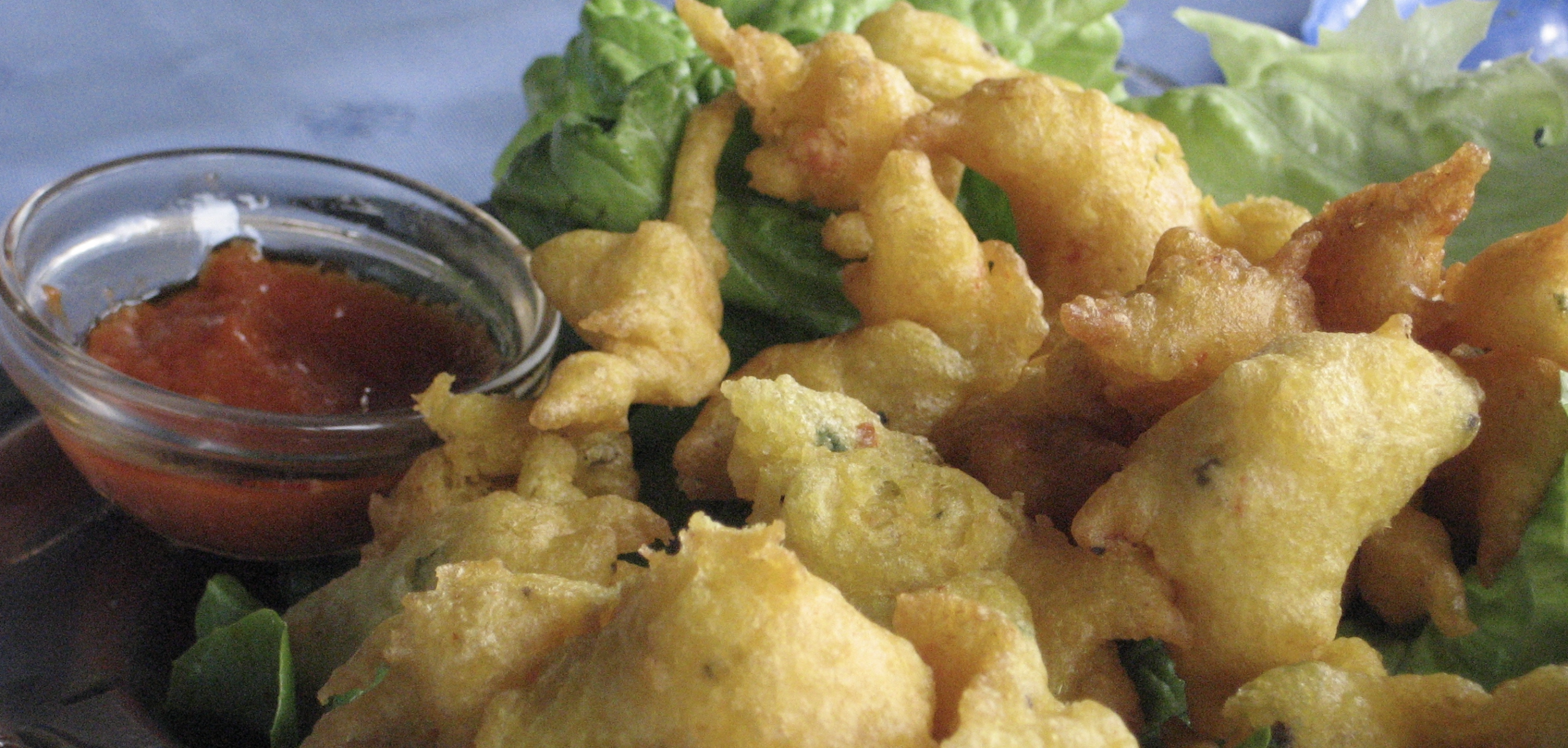 Gros plan sur des pakoras de légumes dorés et croustillants servis sur des feuilles de laitue verte, accompagnés d'un petit verre de sauce rouge.