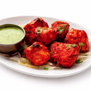 POULET TANDOORI (300g) : Morceaux de poulet tandoori grillés, garnis de coriandre et d'oignons émincés, servis dans une assiette ovale blanche avec un chutney vert.