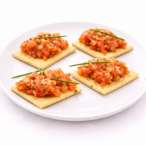 Les TOMATES FONDANTES À LA RICOTTA ET TUILES DE PARMESAN sont élégamment disposées sur une assiette blanche, avec des tomates et de la ricotta sur des chips de parmesan, garnies d'herbes sur un fond blanc.