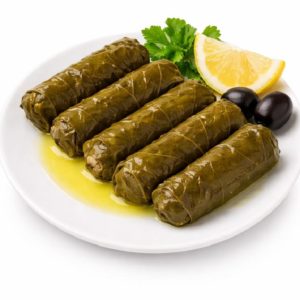 FEUILLES DE VIGNES (Entrée froide) : cinq feuilles de vigne farcies disposées sur une assiette blanche, nappées d'huile d'olive et servies avec deux olives noires, un quartier de citron et du persil. Mini commande : 5 pièces.