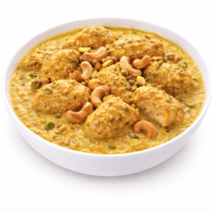 Un bol de POULET PISTACHES (300g) présente un curry jaune crémeux avec des morceaux de poulet, garnis de noix de cajou entières et de pistaches.