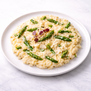 RISOTTO AUX MORILLES ET COPEAUX ET POINTES D'ASPERGES servi dans une assiette blanche, risotto crémeux aux pointes d'asperges et garni de microgreens, sur fond de marbre clair.