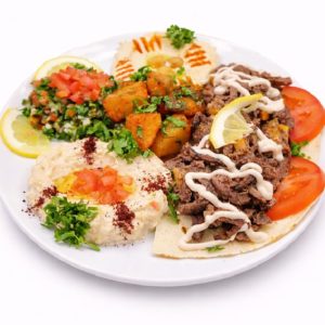 Le CHAWARMA VIANDE DE BOEUF (Plat - Min de commande 5 plats de 300g/Pers) propose un shawarma de bœuf avec sauce blanche, tranches de citron, tomates, taboulé, houmous aux herbes, baba ganoush, pommes de terre assaisonnées et garniture de persil.