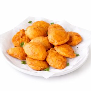 Une assiette blanche tapissée de papier contient une pile d'ALOO PAKORA (minimum de commande 10 pièces 30g/pièce), des pâtisseries frites garnies de petits brins de persil.
