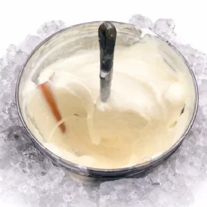 Un bol métallique d'ANIMATION SORBET COCO ANTILLAIS (1h30), crémeux et blanc, avec une cuillère à l'intérieur, repose sur des glaçons pour rester frais.