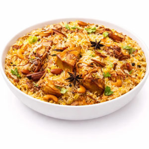 Un bol blanc de BIRIYANI À L'AGNEAU (300 g) est garni et prêt à être servi, avec des morceaux d'agneau visibles, du riz parfumé, de l'anis étoilé, des noix de cajou, de la coriandre et des épices sur un fond blanc.