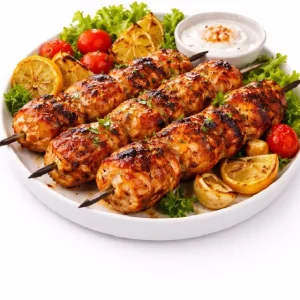 BROCHETTE DE POULET CUITE AU FEU DE BOIS (Barquette de 10 pièces) : savoureuses brochettes grillées servies sur assiette avec laitue, citrons grillés, tomates cerises et un bol de sauce au yaourt.