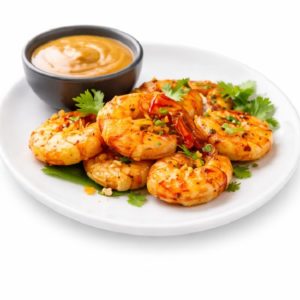 Une portion de CREVETTES SAUCE PIQUANTE (250g/pers) avec des crevettes grillées, des herbes, des flocons de piment rouge et un accompagnement de sauce crémeuse sur une assiette blanche.