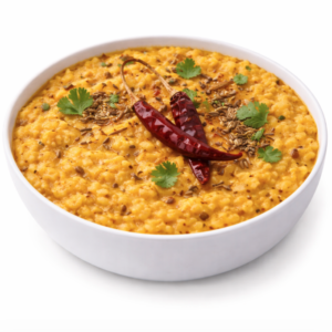 Une portion de DAAL TADKA (250 g) est présentée dans un bol blanc, avec du dal de lentilles jaunes garni de piments rouges séchés, de graines de cumin et de feuilles de coriandre fraîche sur un fond blanc.