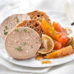 DUO DE FOIE GRAS SUR TOASTS : Tranches de foie gras servies sur du pain grillé avec un assortiment de légumes marinés et une garniture d'herbes, présentées sur un fond blanc.