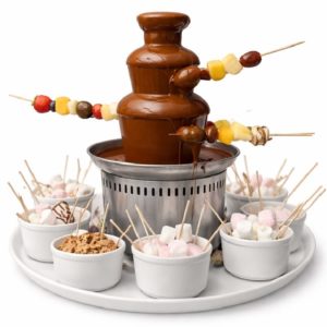 L'ANIMATION FONTAINE A CHOCOLAT propose une fontaine à fondue au chocolat avec des brochettes de fruits à tremper, ainsi que des bols de guimauves, de biscuits et de friandises disposés sur un plateau blanc - une expérience dont vos invités se souviendront.