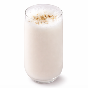 Un verre de 30cl de LASSI NATURE, rempli d'une boisson blanche mousseuse et agrémenté d'épices moulues, sur un fond blanc uni.