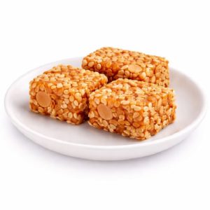 Trois pièces rectangulaires de NOUGAT CHINOIS (Barquette de 10 pièces) avec cacahuètes et graines de sésame sont disposées sur une assiette blanche sur fond blanc.