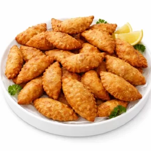 Une assiette blanche contient le PASTEL DE VIANDE doré et croustillant (minimum de commande 10 pièces), garni de coriandre fraîche et de quartiers de citron sur le côté.