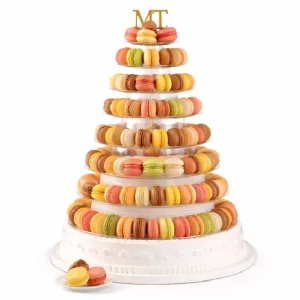 Le PIÉCE MONTÉE PYRAMIDE DE 91 MACARONS se compose d'un stand haut et étagé présentant des macarons vibrants aux saveurs assorties, surmontés des initiales MT dorées et complétés par une petite assiette de macarons supplémentaires devant la base blanche.