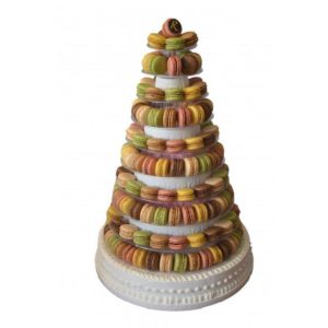 La PIÉCE MONTÉE PYRAMIDE DE 191 MACARONS est une haute tour en forme de cône qui présente des macarons colorés de couleur verte, jaune, rose, marron et beige, empilés avec art sur des gradins circulaires sur une base décorative blanche.