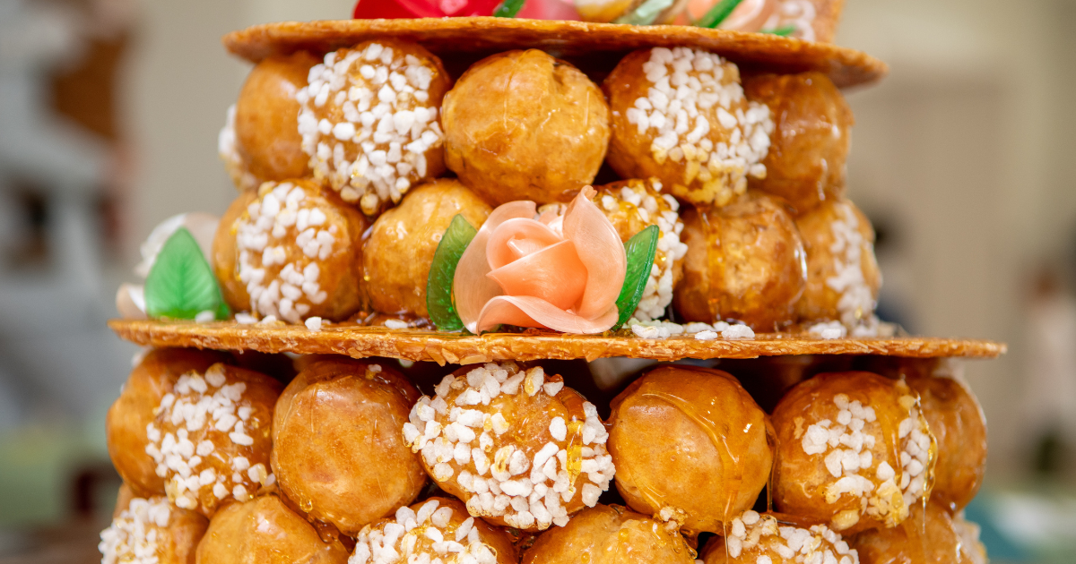 Gros plan sur un croquembouche, un dessert français composé de feuilletés fourrés à la crème empilés dans une tour, décorés de caramel, de perles de sucre et de fleurs en sucre roses et vertes.