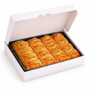 Une boîte blanche contient le PLATEAU DE 16 BAKLAVAS - des pâtisseries dorées et feuilletées soigneusement disposées et garnies de pistaches concassées.