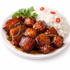 PORC AU CARAMEL (250g/pers) : Tendre poitrine de porc braisée et caramélisée dans une sauce brillante, servie avec du riz blanc, des tranches de piment rouge et de la coriandre fraîche.