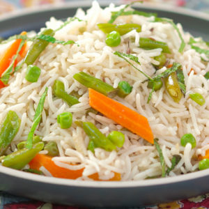 Gros plan sur le RIZ AUX LÉGUMES, qui présente du riz basmati moelleux accompagné de haricots verts, de carottes et de pois verts, servi sur une nappe à motifs.