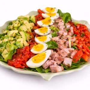 SALAD COMPOSÉE (Minimum de commande de 5 pers/200g/) : salade en rangées avec avocat, tomates, œufs durs, jambon cuit en dés et jeunes pousses, le tout parsemé d'herbes aromatiques.