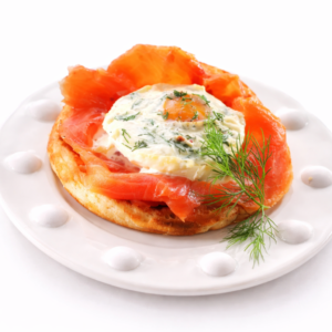 BLINIS AU OEUFS DE SAUMON : Blinis moelleux garnis d'œufs de saumon, de fromage frais aux herbes, de tranches d'œufs durs et d'aneth frais, servis dans une assiette blanche.