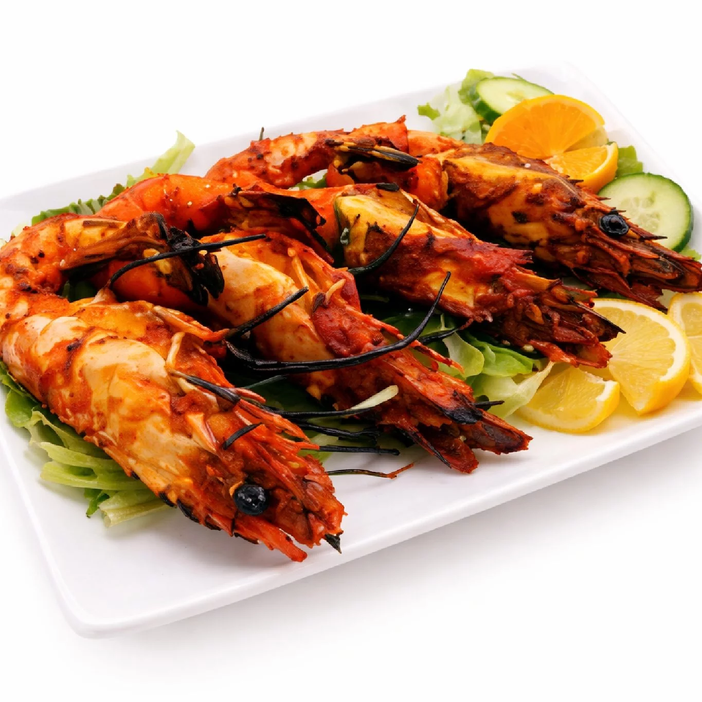 TANDOORI GAMBAS (350g) : Trois grosses crevettes grillées sur de la laitue, servies avec des tranches de concombre, des quartiers d'orange et des tranches de citron sur une assiette rectangulaire blanche.