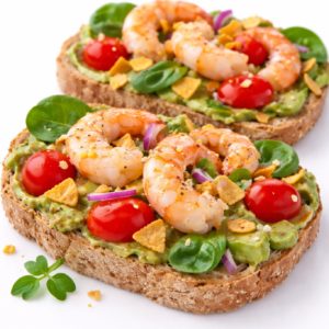TOAST DE PLANTAIN À L'AVOCAT ET AUX CREVETTES (Plateau de 10 pièces) : des toasts de plantain garnis d'avocat, crevettes, tomates cerises, épinards, oignon rouge et herbes fraîches pour un apéritif savoureux.